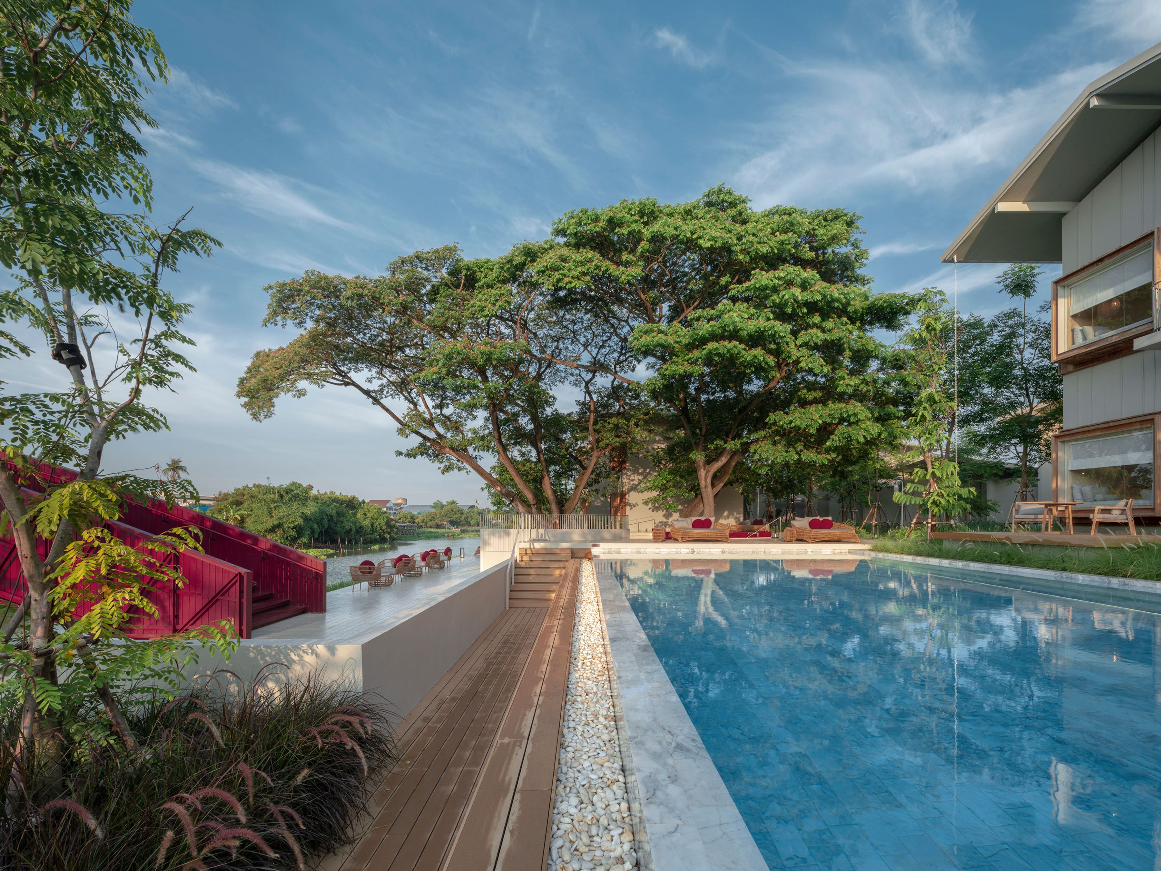 A swimming pool with a wooden deck, surrounded by trees and outdoor seating.