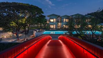 Ein modernes Hotel mit Schwimmbad, einer rot beleuchteten Brücke und üppigem Grün.