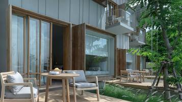 Un área de estar moderna al aire libre con mobiliario de madera, un acceso por puerta de vidrio y un balcón con barandilla blanca.