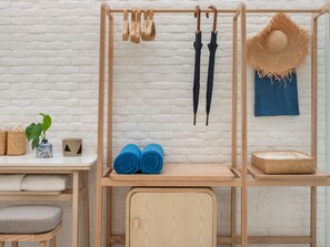 A wooden shelf unit with rolled towels, a hat, and umbrellas against a white brick wall. - sala bang pa-in, a Member of Design Hotels (Bang Pa-in)