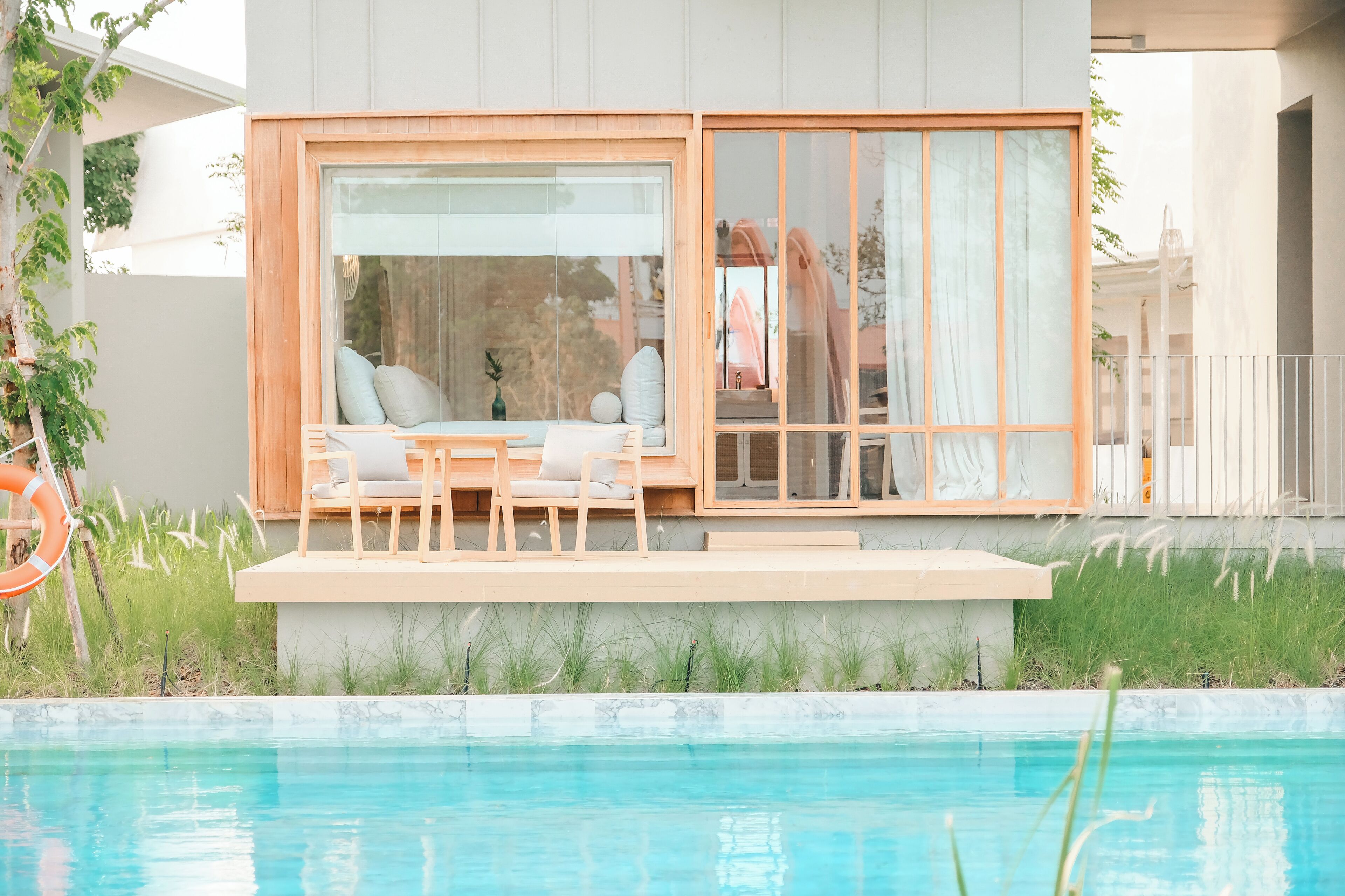 Un espace de détente extérieur moderne avec piscine, comprenant une terrasse en bois, des fauteuils confortables et une structure en verre.