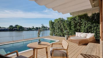 Una terraza de madera con piscina, sillas de descanso y vistas a un cuerpo de agua.