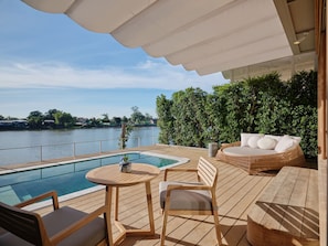A wooden deck with a pool, lounge chairs, and a view of a body of water.