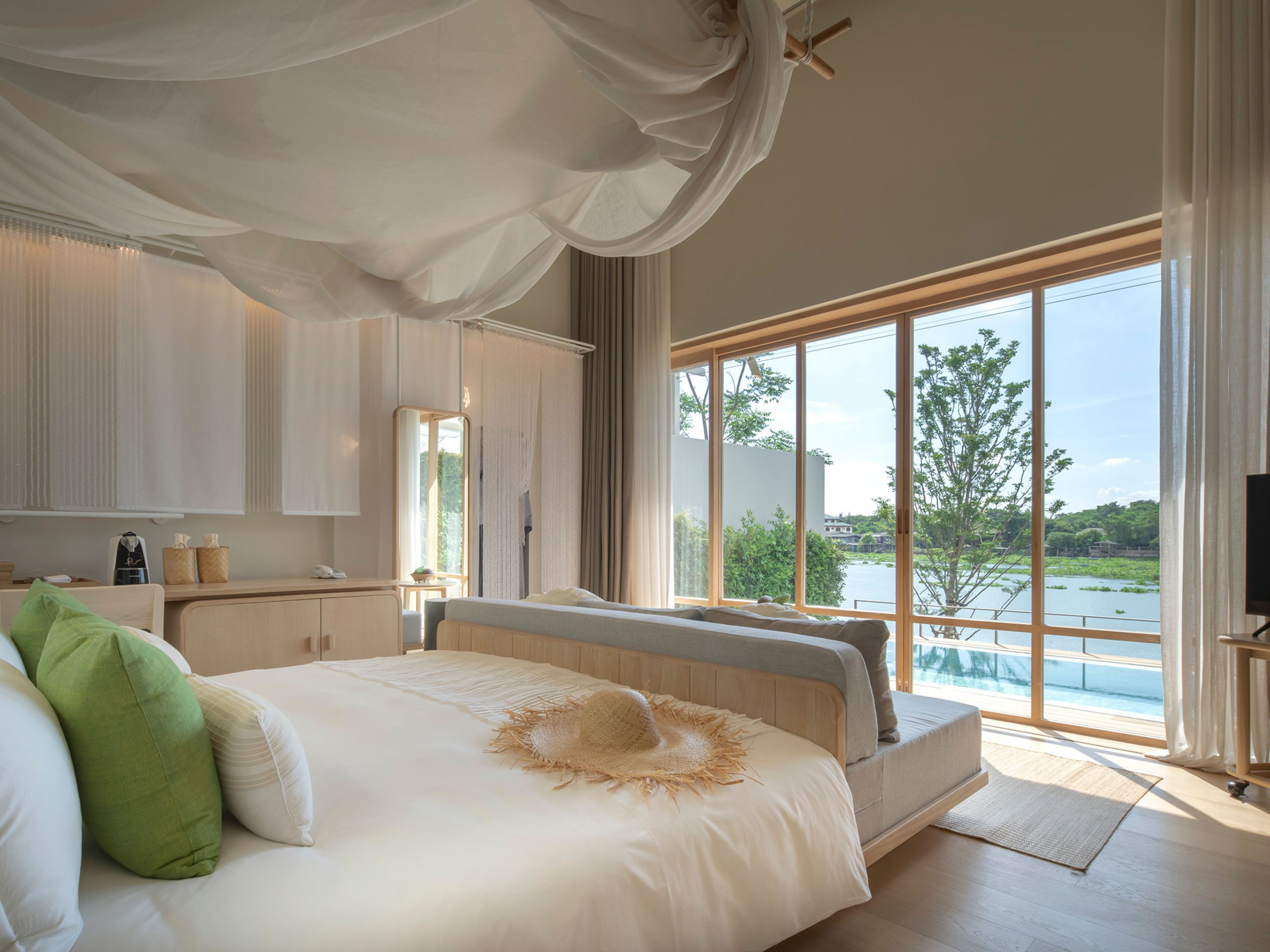 A bedroom with a large bed, a view of a body of water, and a window with curtains.