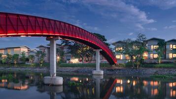 Uma ponte vermelha sobre águas calmas, com edifícios ao fundo.