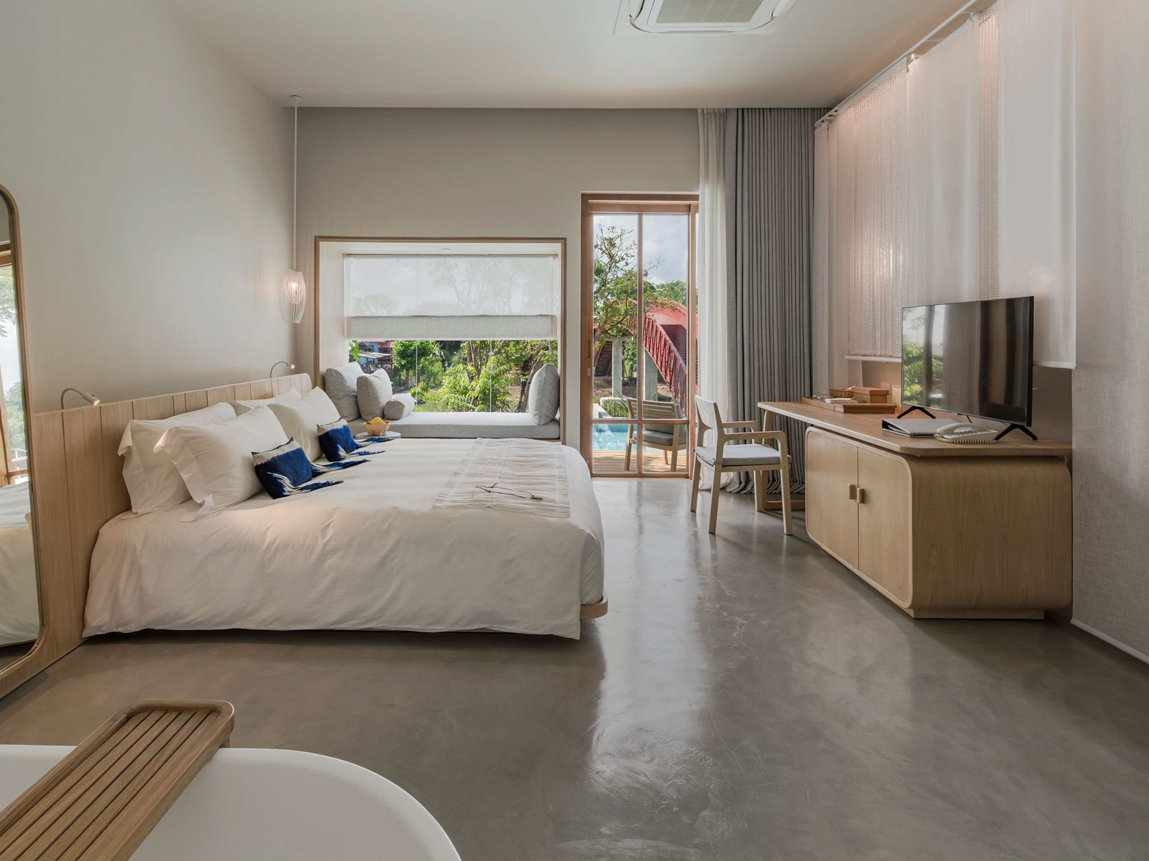Ein Hotelzimmer mit Bett, Schreibtisch mit Fernseher und Blick ins Freie.