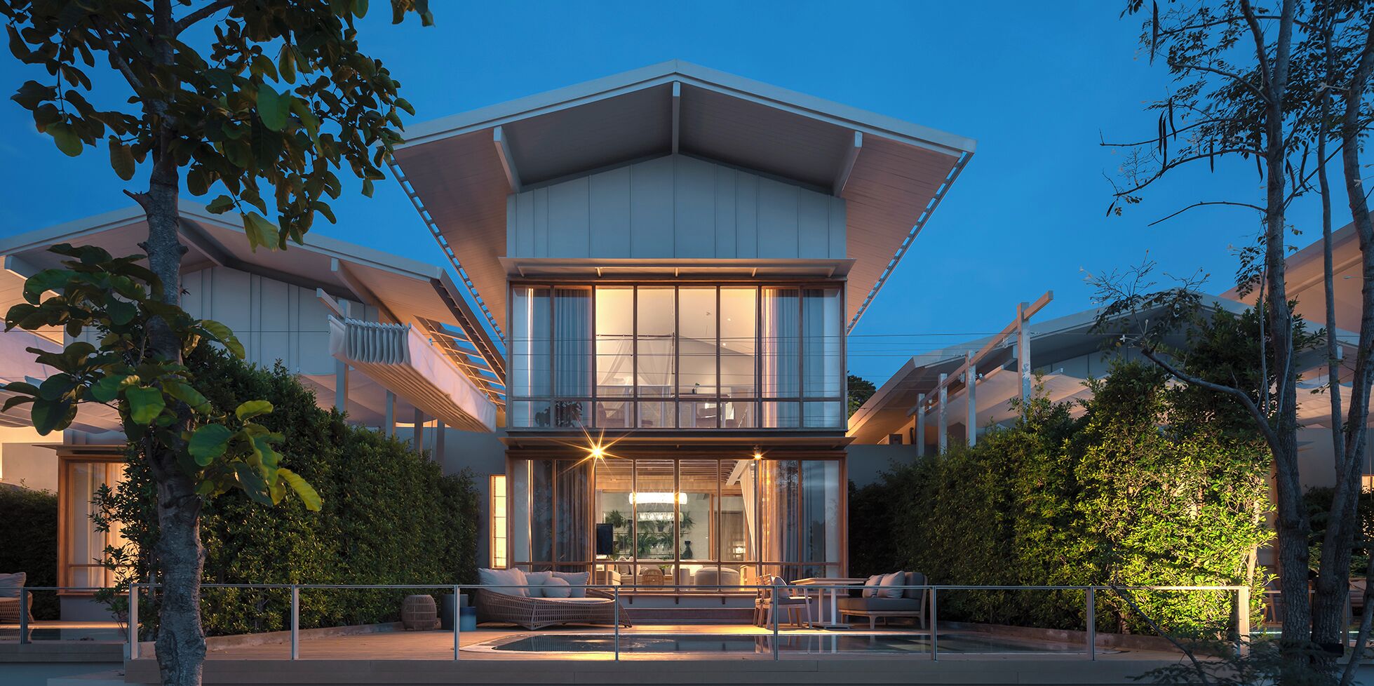 Une maison moderne à deux étages, dotée d’un toit plat, de grandes fenêtres et d’un balcon.
