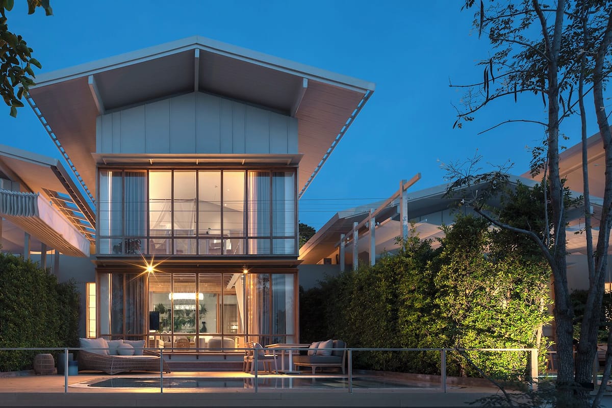 A modern two-story house with a flat roof, large windows, and a balcony.
