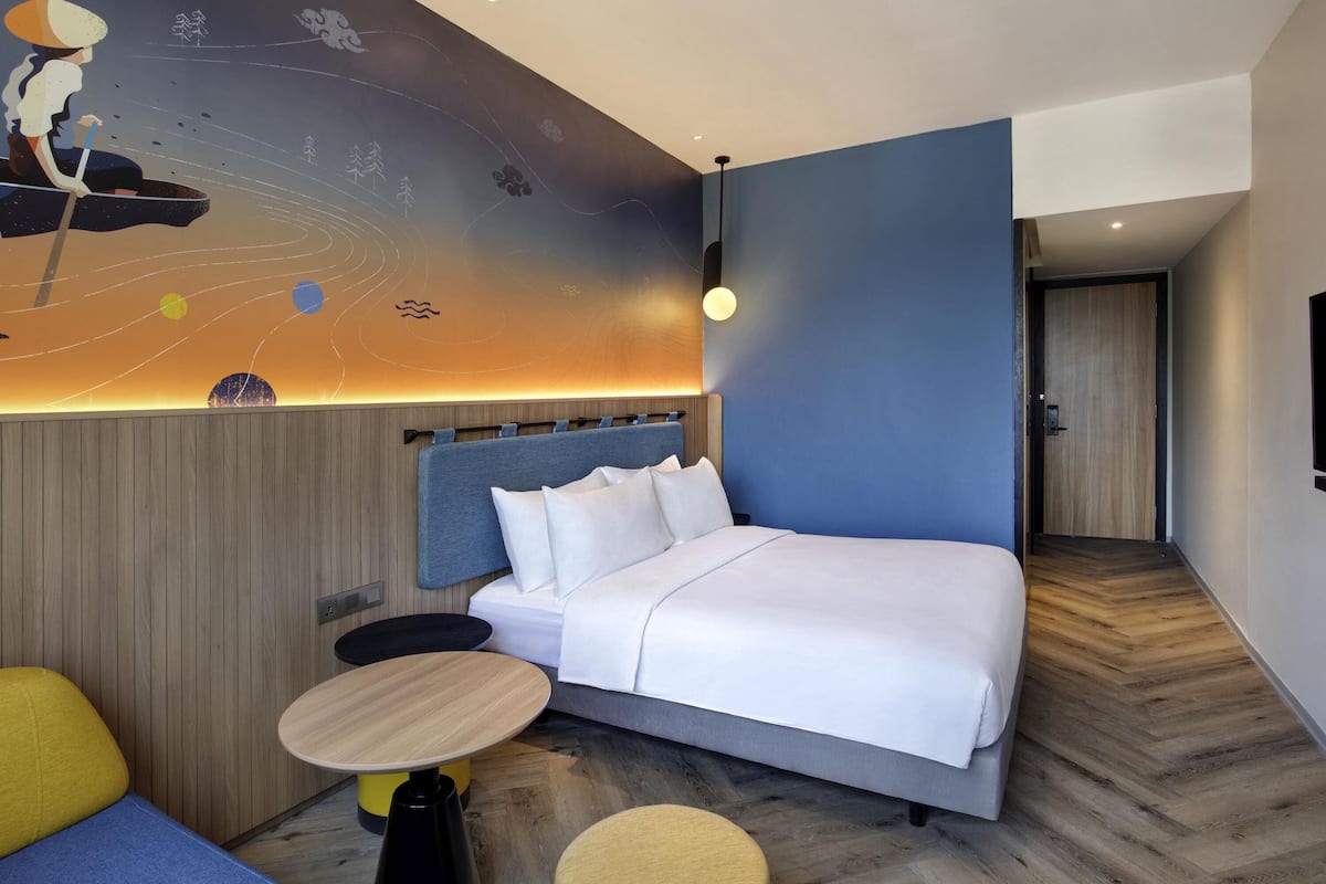 A modern hotel room with a large bed, a small round table, and a colorful mural on the wall.