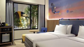 Habitación de hotel con una cama grande, un escritorio, una silla, una mesita pequeña y un ventanal con vistas a plantas de bambú.