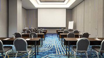 A conference room with a large projection screen, rows of tables with chairs, and a patterned carpet.