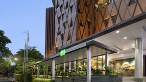 A modern building with a geometric facade, a covered entrance, and a landscaped area with stairs leading up to the entrance. - Ibis Styles Semarang Simpang Lima (Semarang)