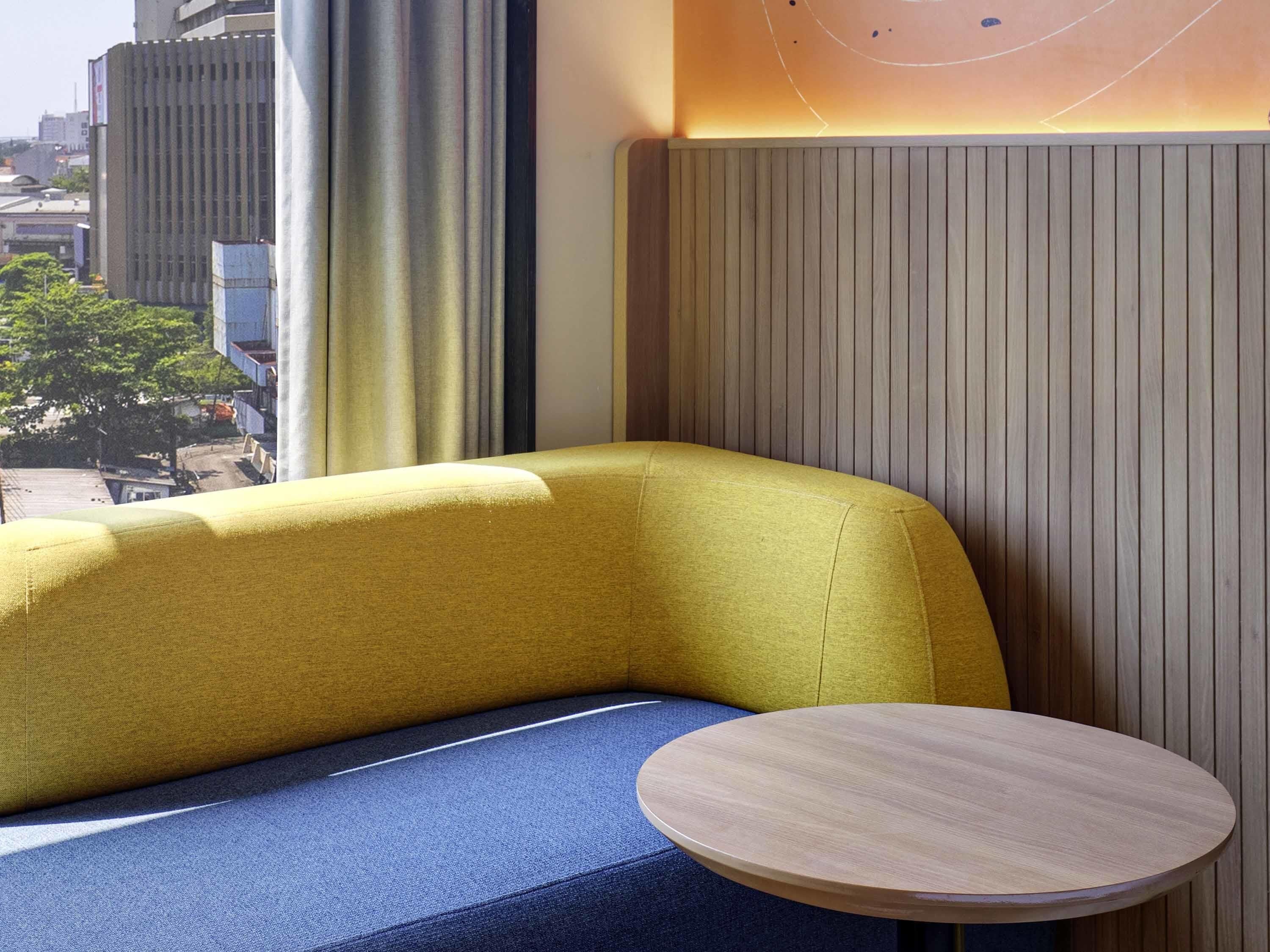 Un rincón con asientos que incluye un banco tapizado en amarillo y una mesa redonda de madera.