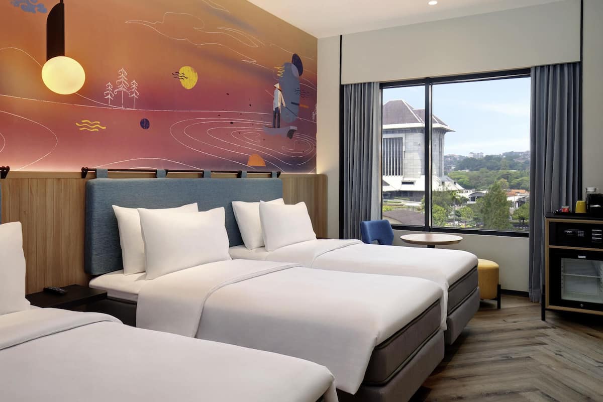 A hotel room with two beds, a desk, a chair, and a large window with a city view.