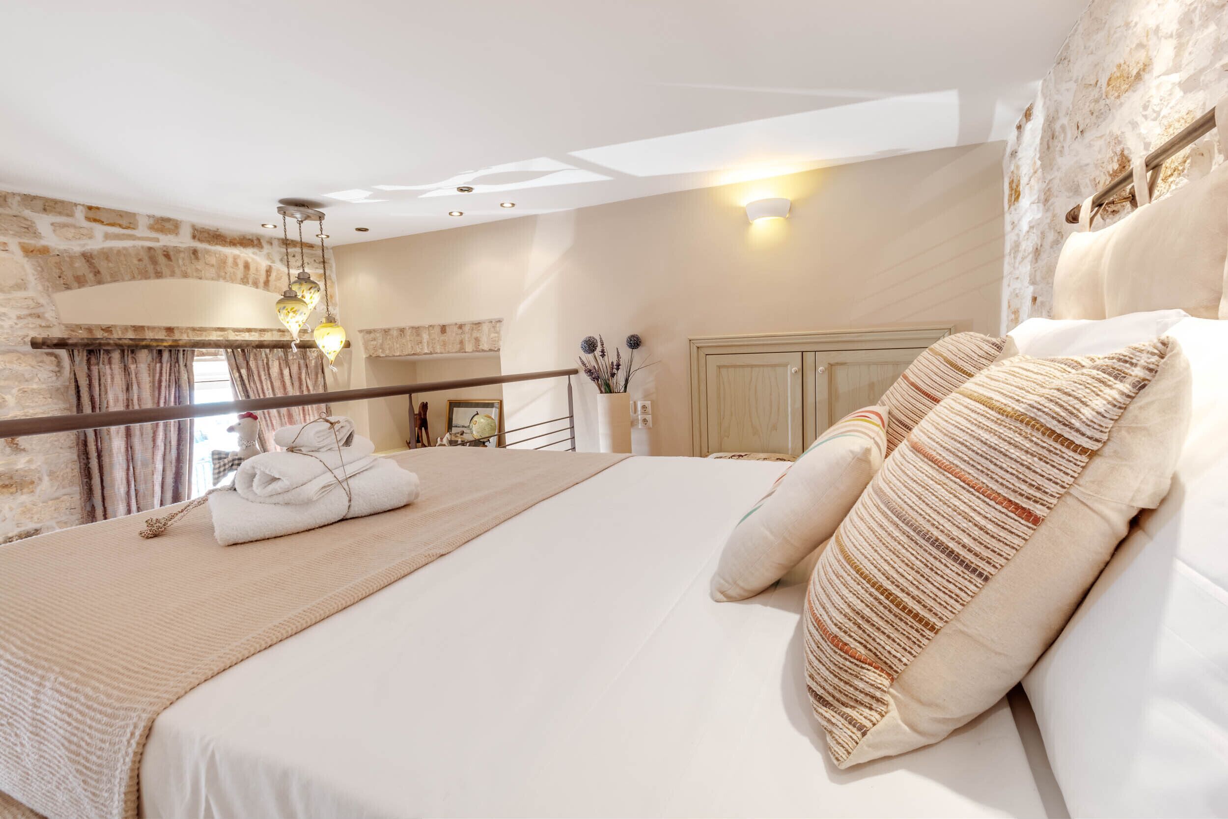 A bedroom with a large bed, a wooden headboard, a stone wall, and a hanging light fixture.