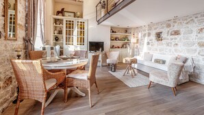 A spacious living room with a high ceiling, a dining area with wicker chairs, a white sofa, and a stone wall. - Mouragia Loft - Waterfront Old Corfu Town (Corfu)
