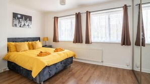 Un dormitorio con cama, mesita de noche, lámpara, ventana con cortinas, radiador y espejo.