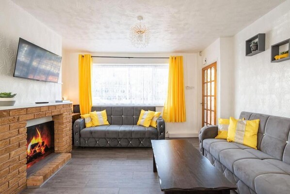 Una sala de estar con chimenea, dos sofás, una mesa de centro y un televisor montado en la pared.