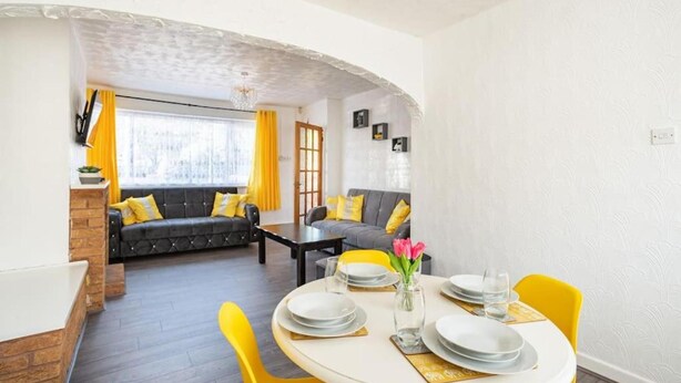 Comedor con mesa redonda dispuesta para cuatro personas, sillas amarillas y un florero con flores.