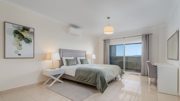 A modern bedroom with a bed, bedside tables, a desk, a chair, a large window, and a ceiling light. - Casa Saudade, semidetached house with Jacuzzi near Ferragudo (Carvoeiro)