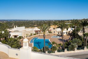 A resort with multiple swimming pools, palm trees, and a view of the surrounding landscape.