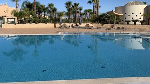 A swimming pool with lounge chairs and palm trees, surrounded by a building with a dome and a beige facade. - Casa Saudade, semidetached house with Jacuzzi near Ferragudo (Carvoeiro)