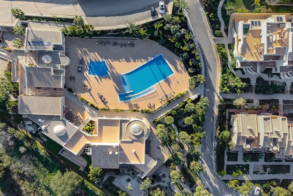 An aerial view of a resort with a large swimming pool, multiple buildings, and landscaped areas.