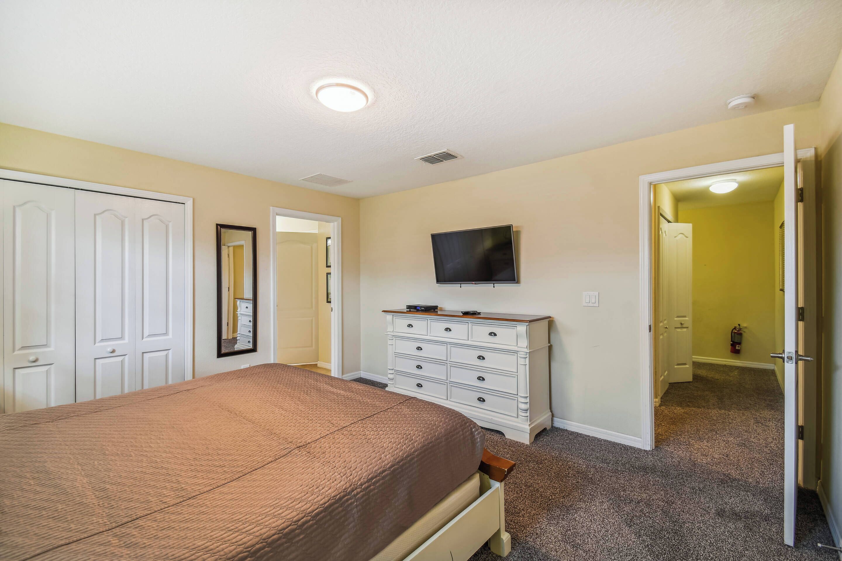 A bedroom with a bed, dresser, television, and a door leading to another room.