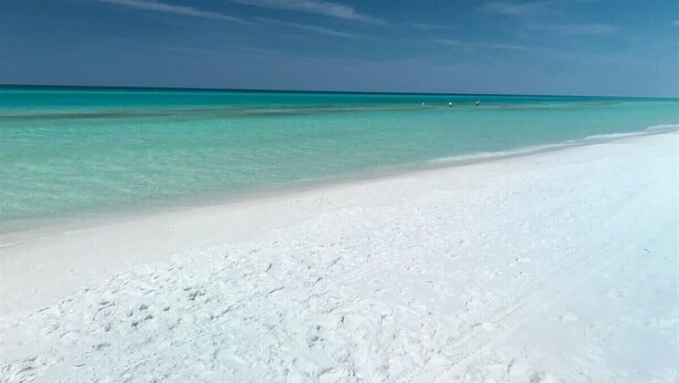 A beach with white sand and clear turquoise water.