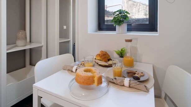 Una mesa de desayuno con un donut, un croissant y jugo, una planta cerca de la ventana, y una vista de un puente al exterior.