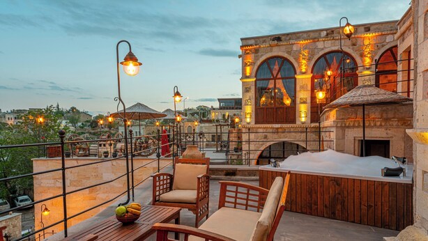 A rooftop terrace with wooden furniture, a hot tub, and stone architecture. - Capp Royal Cave Hotel (Ürgüp)