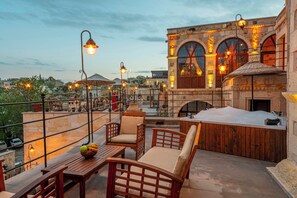 A rooftop terrace with wooden furniture, a hot tub, and stone architecture. - Capp Royal Cave Hotel (Ürgüp)