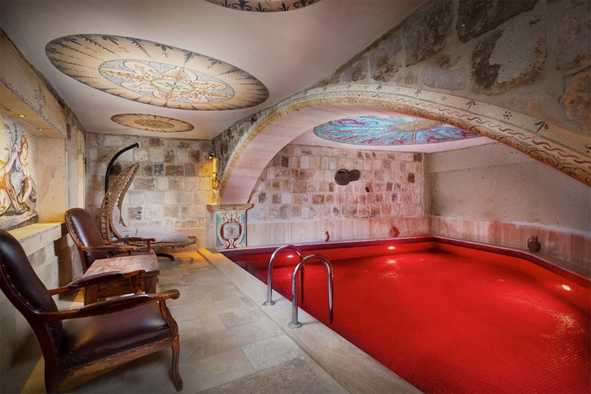 A spa area with a red hot tub, stone walls, and a ceiling with intricate designs.