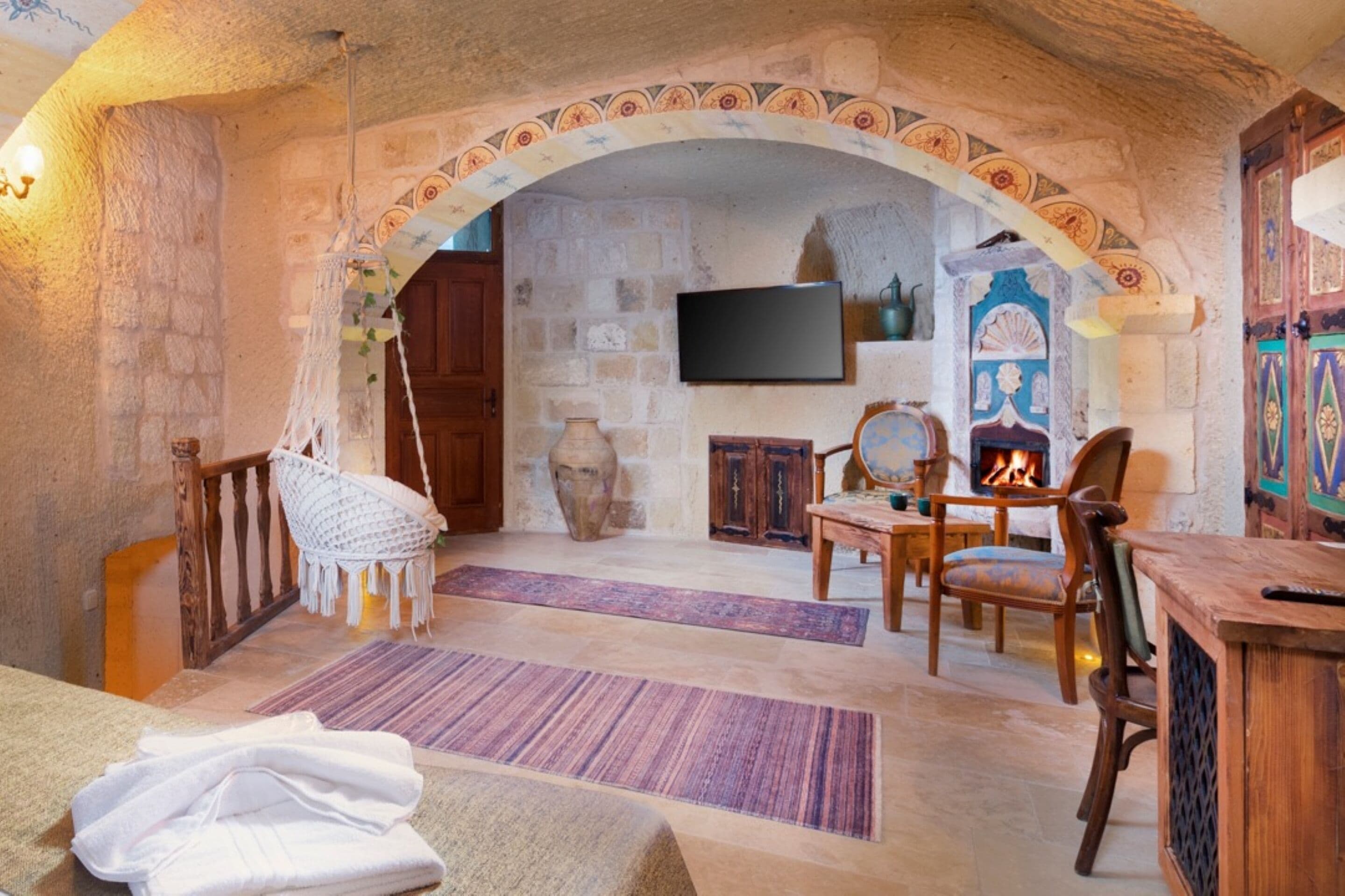 A cozy room with a stone archway, a fireplace, wooden furniture, and a flat-screen TV mounted on the wall.