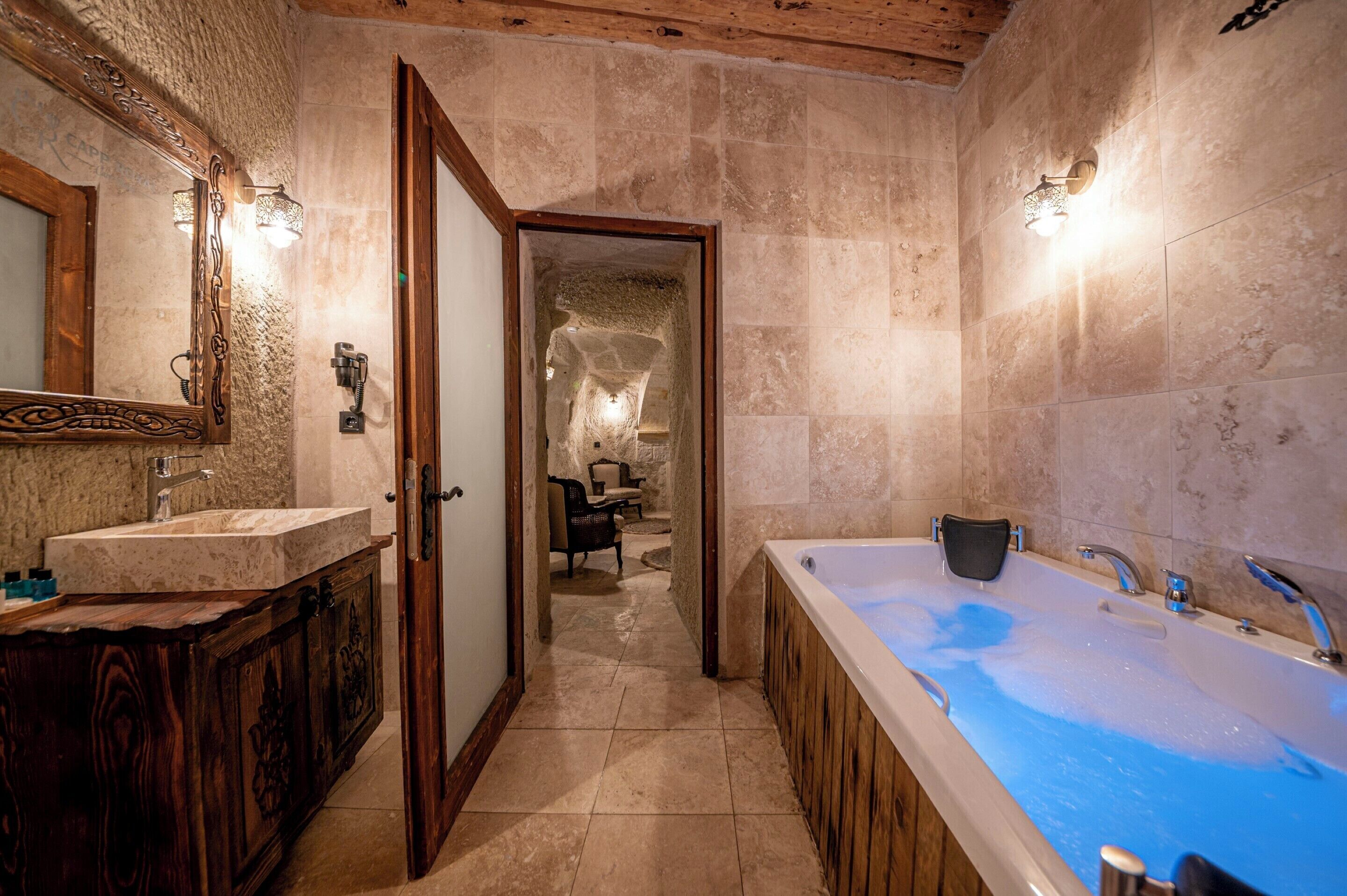 A bathroom with a large bathtub, a wooden vanity with a mirror, and a stone wall.