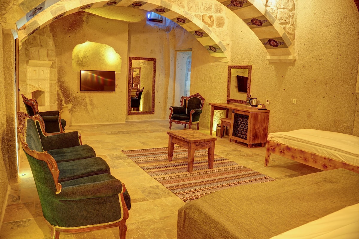 A room with a bed, a chair, a table, a mirror, and a stone wall.