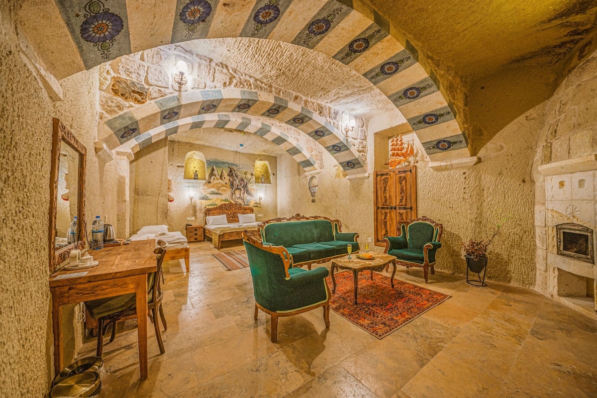 A cozy room with a stone fireplace, a wooden table, and green upholstered chairs.