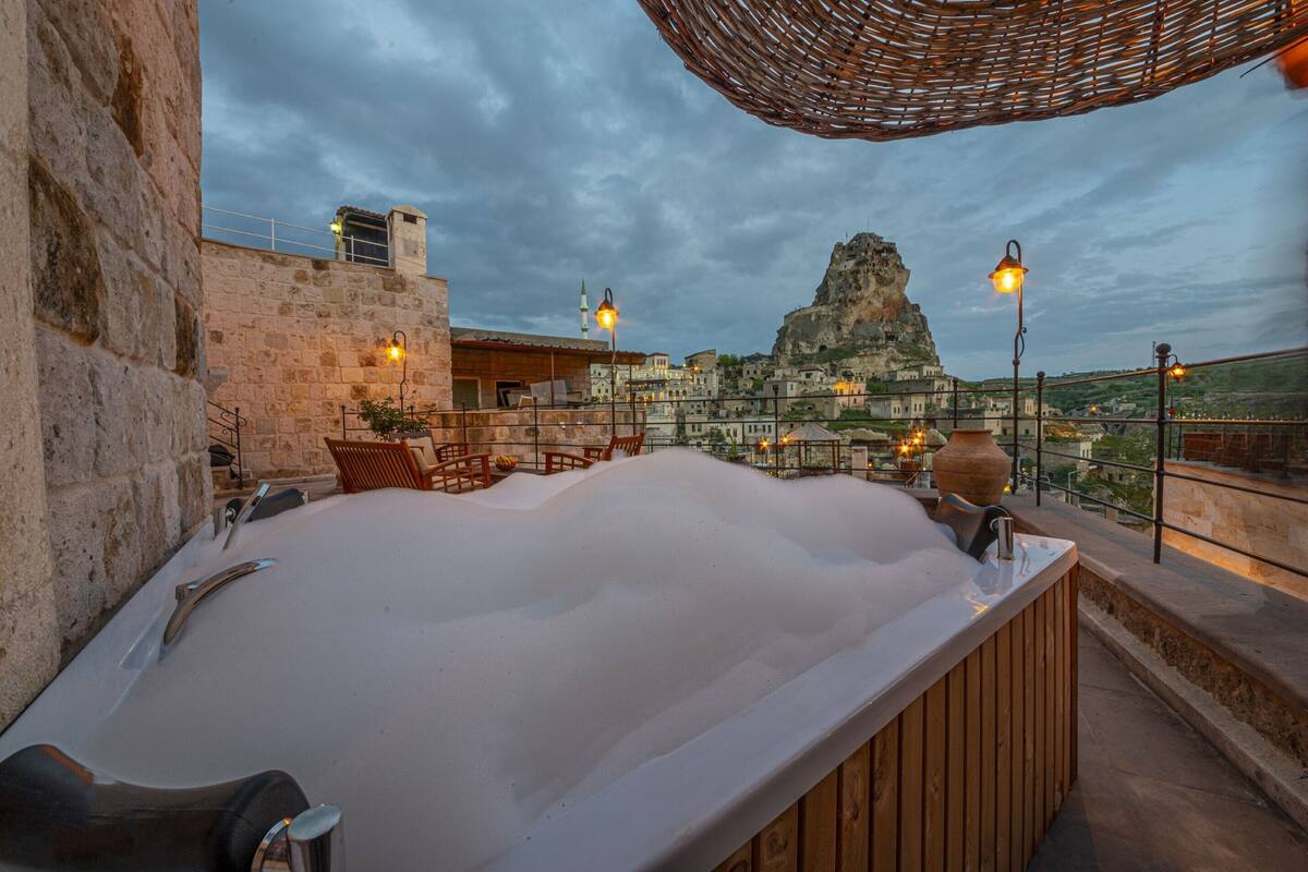 A rooftop terrace with a large bathtub, stone walls, and a view of a mountain.