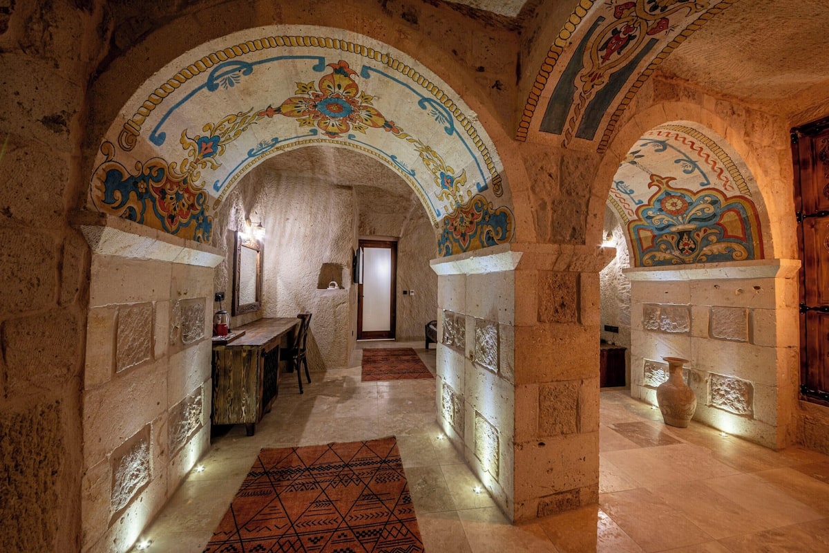 A corridor with stone walls and colorful arches, leading to a room with a wooden door.