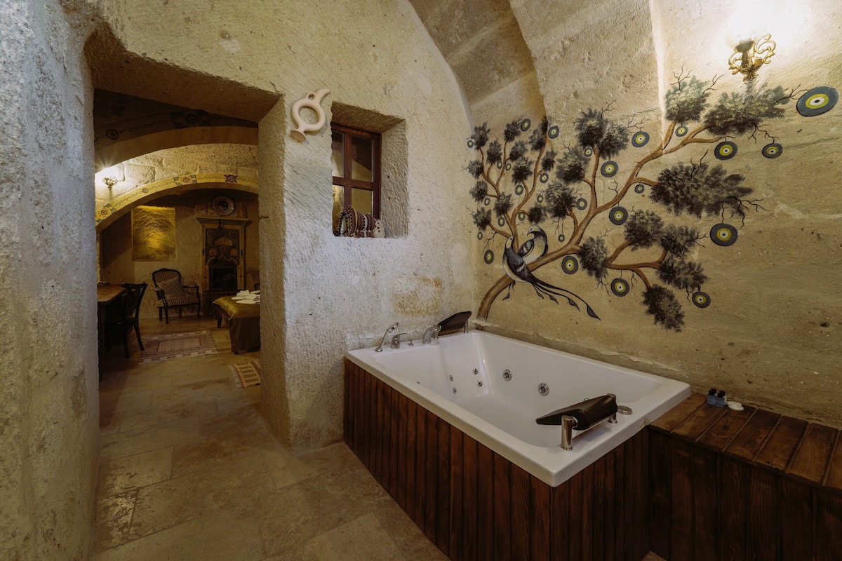 A rustic bathroom with a wooden bathtub, a stone wall, and a tree mural.