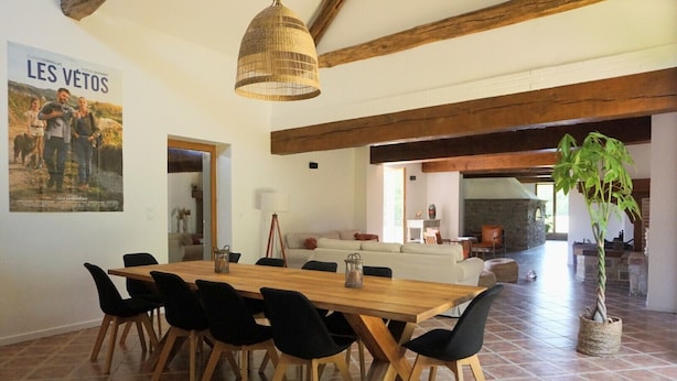 A dining area with a wooden table and black chairs, a hanging light fixture, and a poster on the wall.