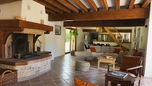 A spacious living area with a stone fireplace, wooden beams, a sofa set, and a dining table.