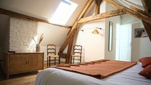 A cozy attic bedroom with a sloped ceiling, a white bed, a wooden dresser, and two chairs.