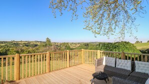 Une terrasse en bois avec un canapé en osier et une table ronde, offrant une vue sur un paysage verdoyant.