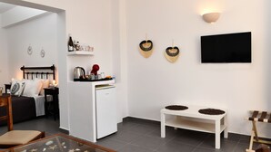 A modern living room with a glass coffee table, a white sofa, a small white table, and a white cabinet with a wine bottle and glasses. - Villa Mare Angelica (Santorini)
