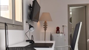 A modern room with a desk, laptop, monitor, lamp, and a small refrigerator. - Villa Mare Angelica (Santorini)