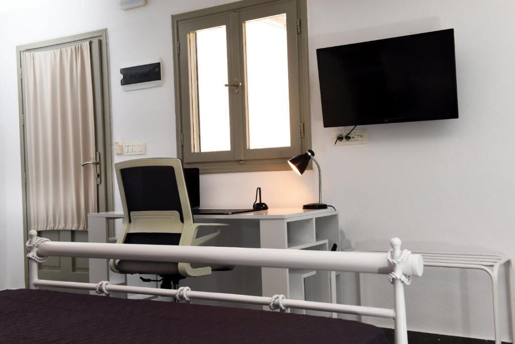 A hospital room with a bed, a desk with a chair, a TV, a window, and a radiator.