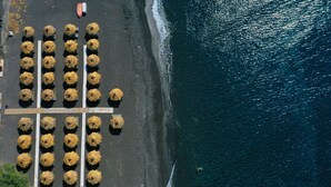 An aerial view of a beach with rows of sun loungers aligned parallel to the shoreline. - Villa Mare Angelica (Santorini)