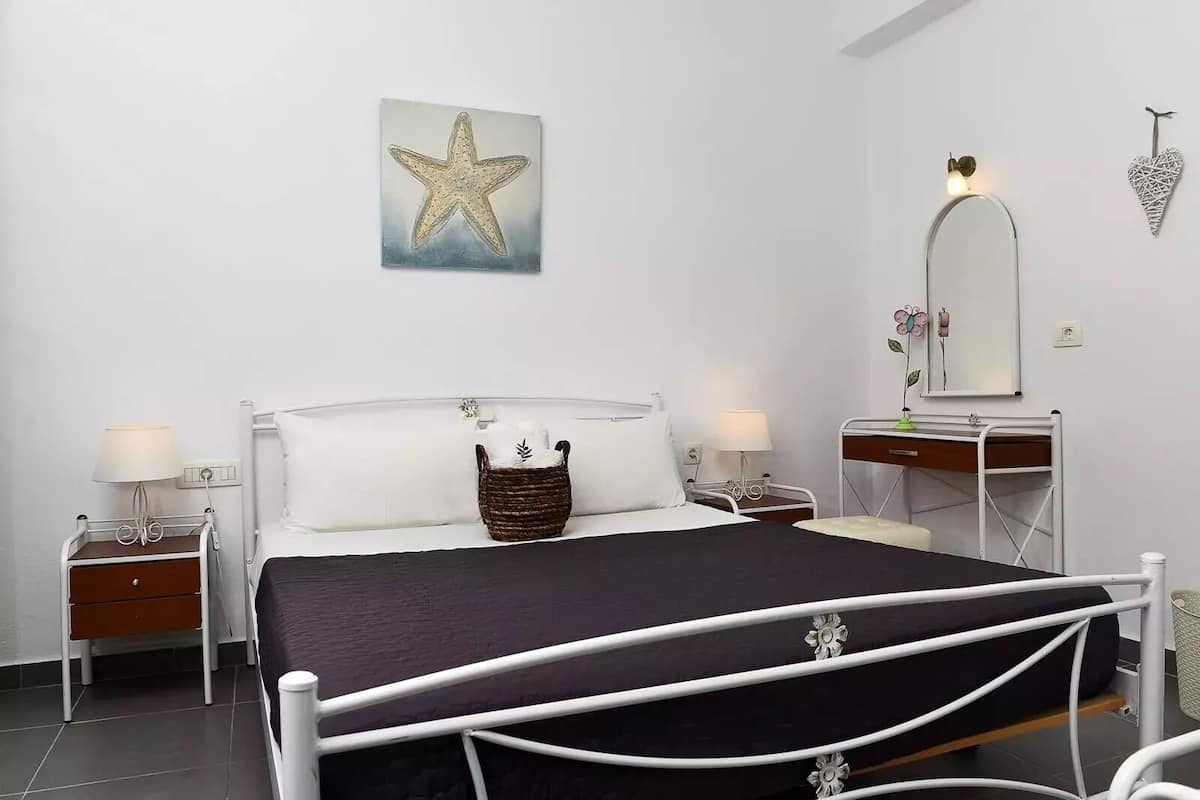 Habitación de hotel con una cama, dos mesitas de noche, un tocador, un aparador, un espejo y una obra de arte con forma de estrella de mar en la pared.