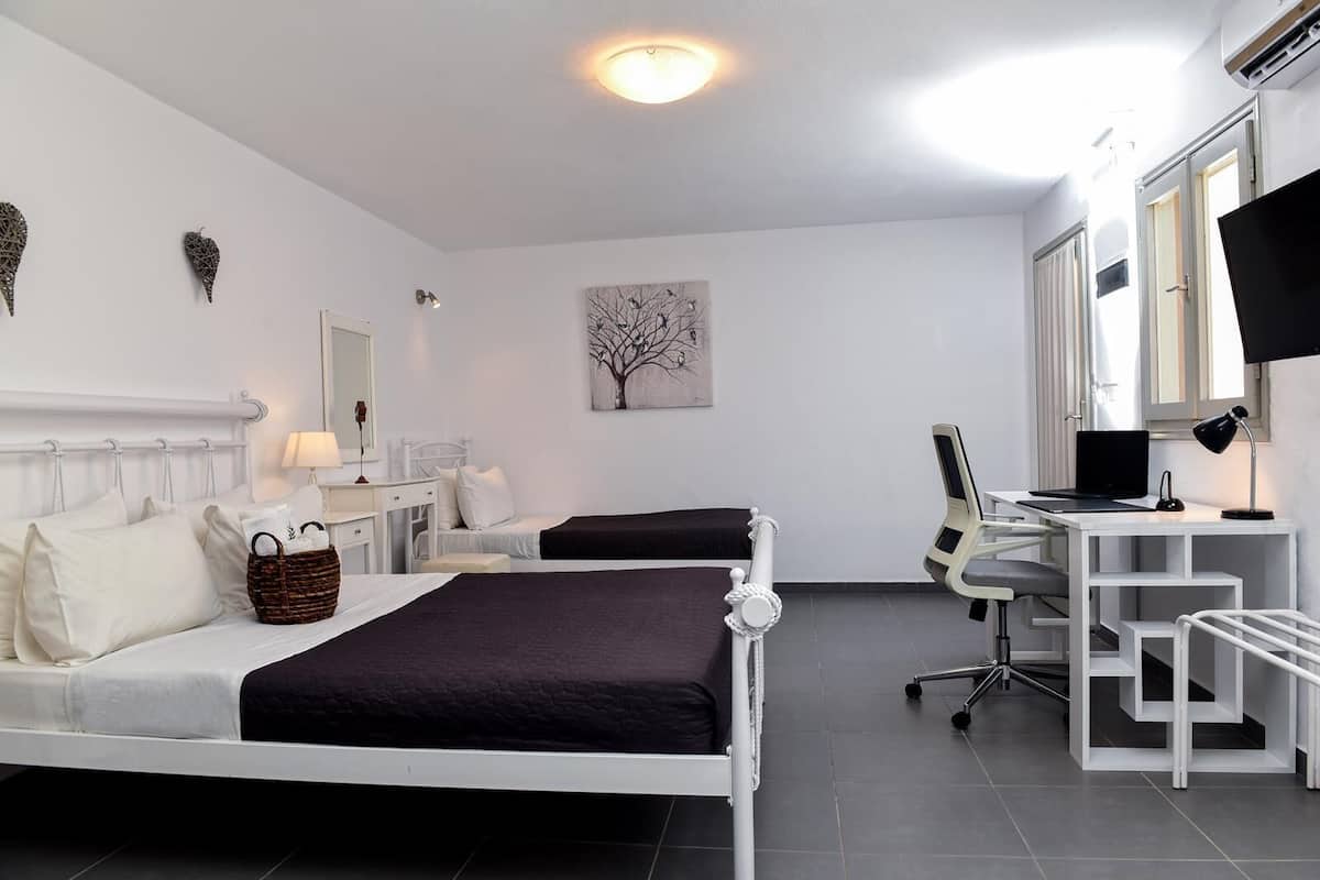 Una habitación de hotel moderna con dos camas, un escritorio con una computadora portátil, una silla, una lámpara de escritorio, un televisor montado en la pared y un cuadro.